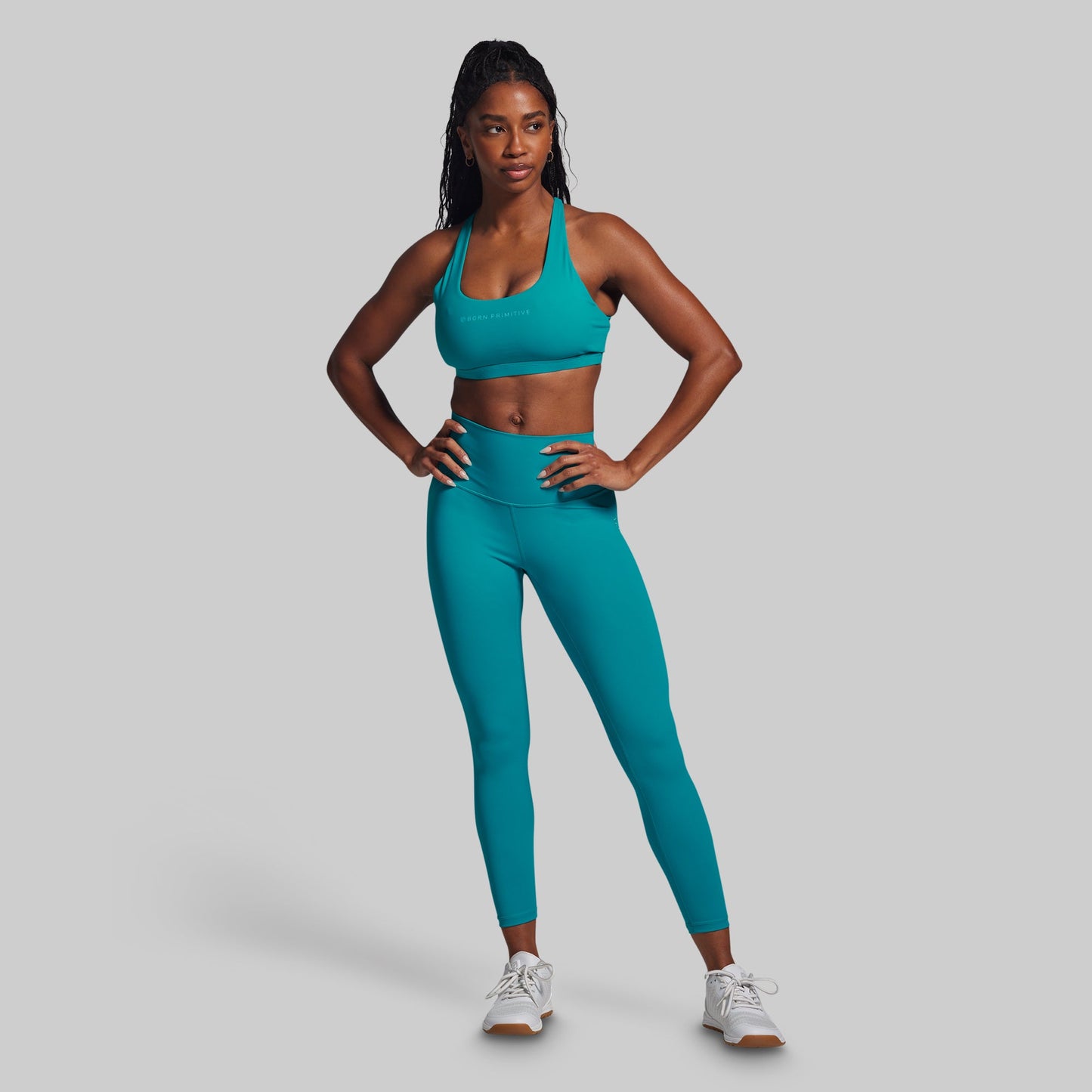 Person wearing a teal sports bra and leggings set on a gray background