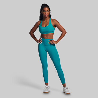 Person wearing a teal sports bra and leggings set on a gray background