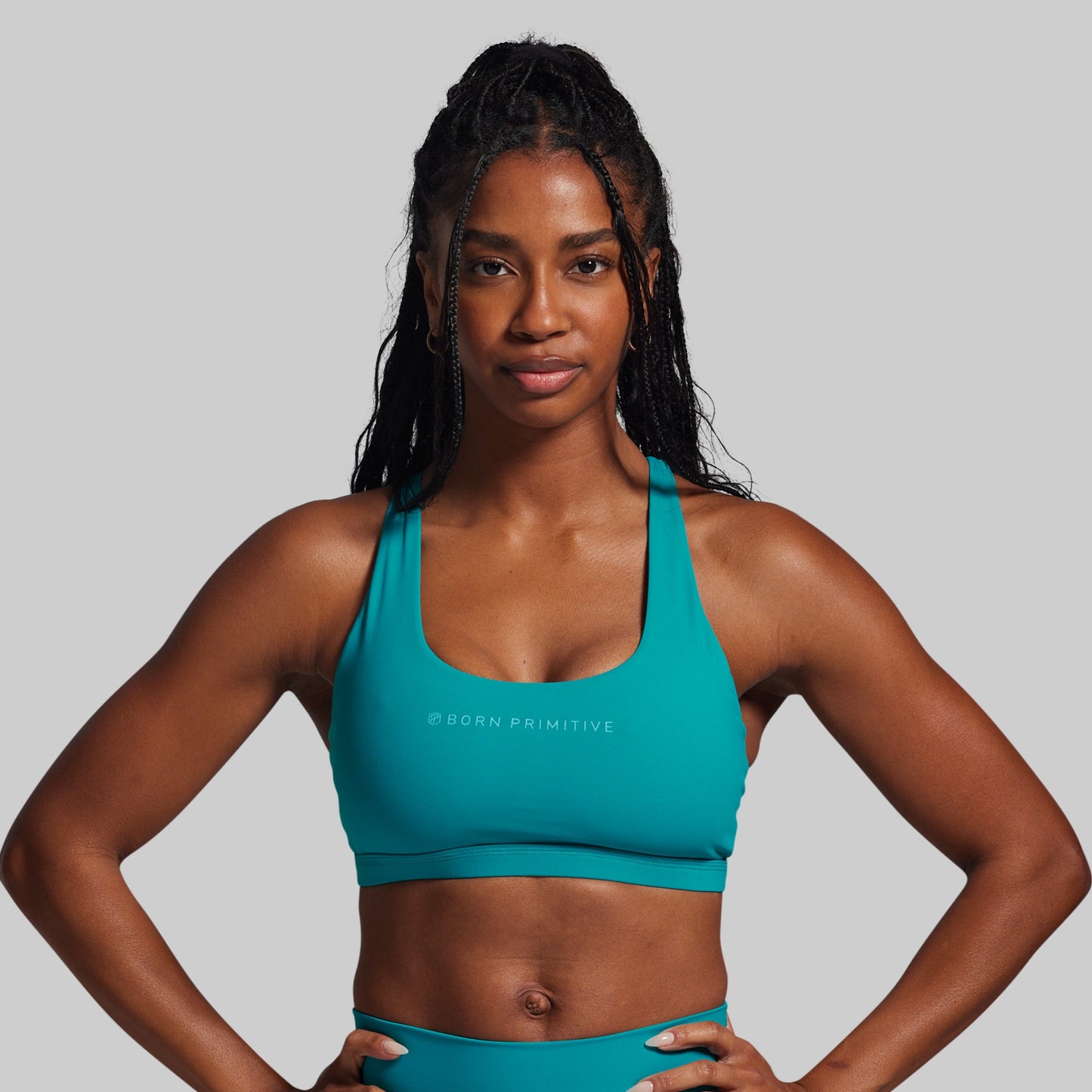 Woman wearing a teal sports bra and shorts with a gray background