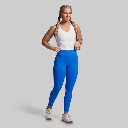 Woman wearing blue leggings and a white tank top on a gray background