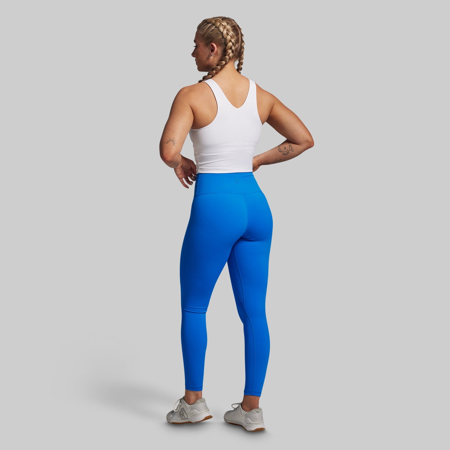 Person wearing blue leggings and a white tank top on a gray background