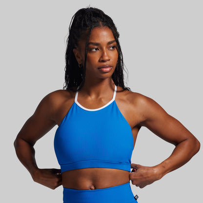 Woman wearing a blue sports bra and leggings on a gray background
