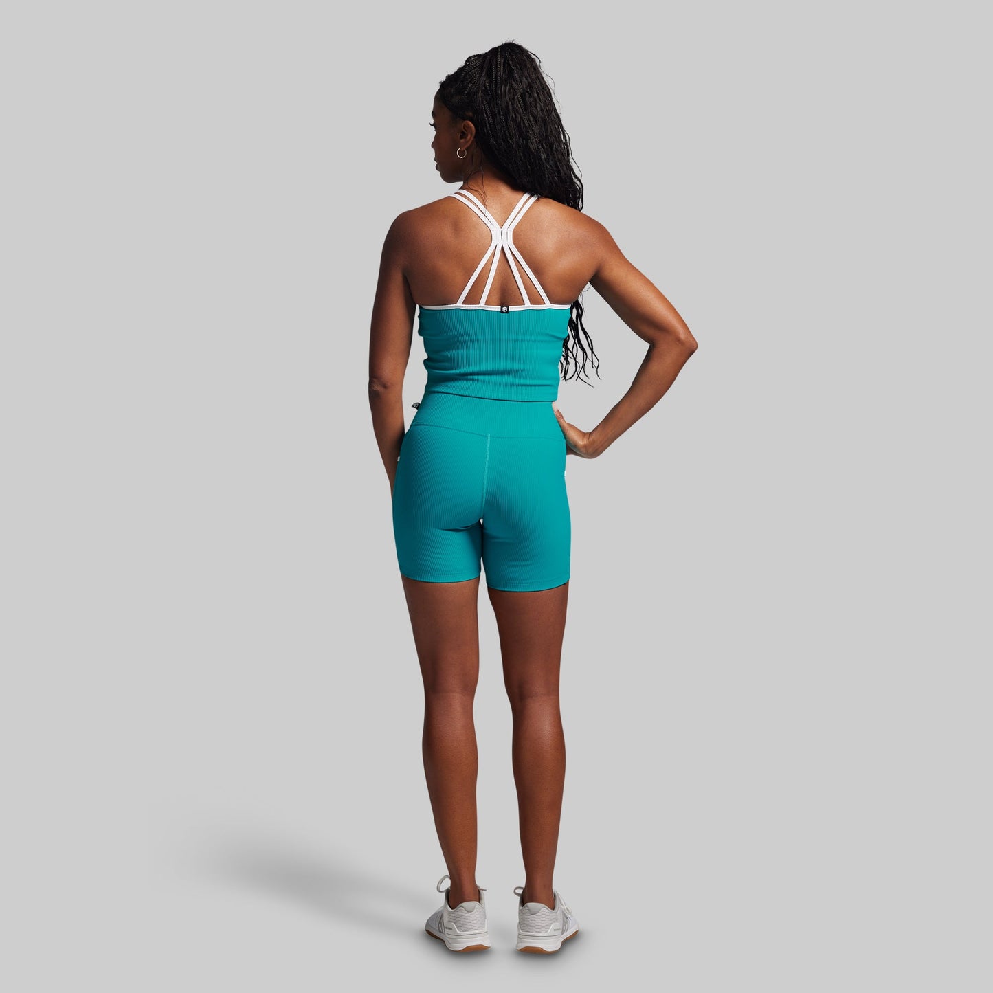 Person wearing a teal athletic outfit with white straps on a gray background