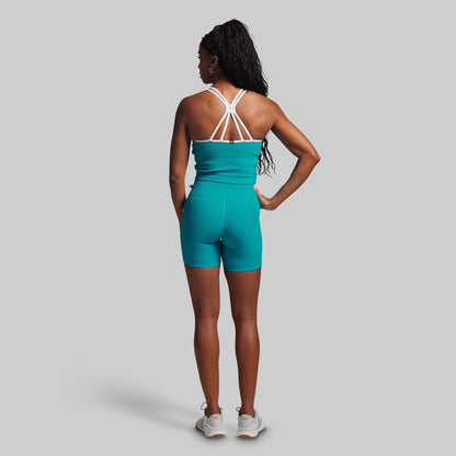 Person wearing a teal athletic outfit with white straps on a gray background