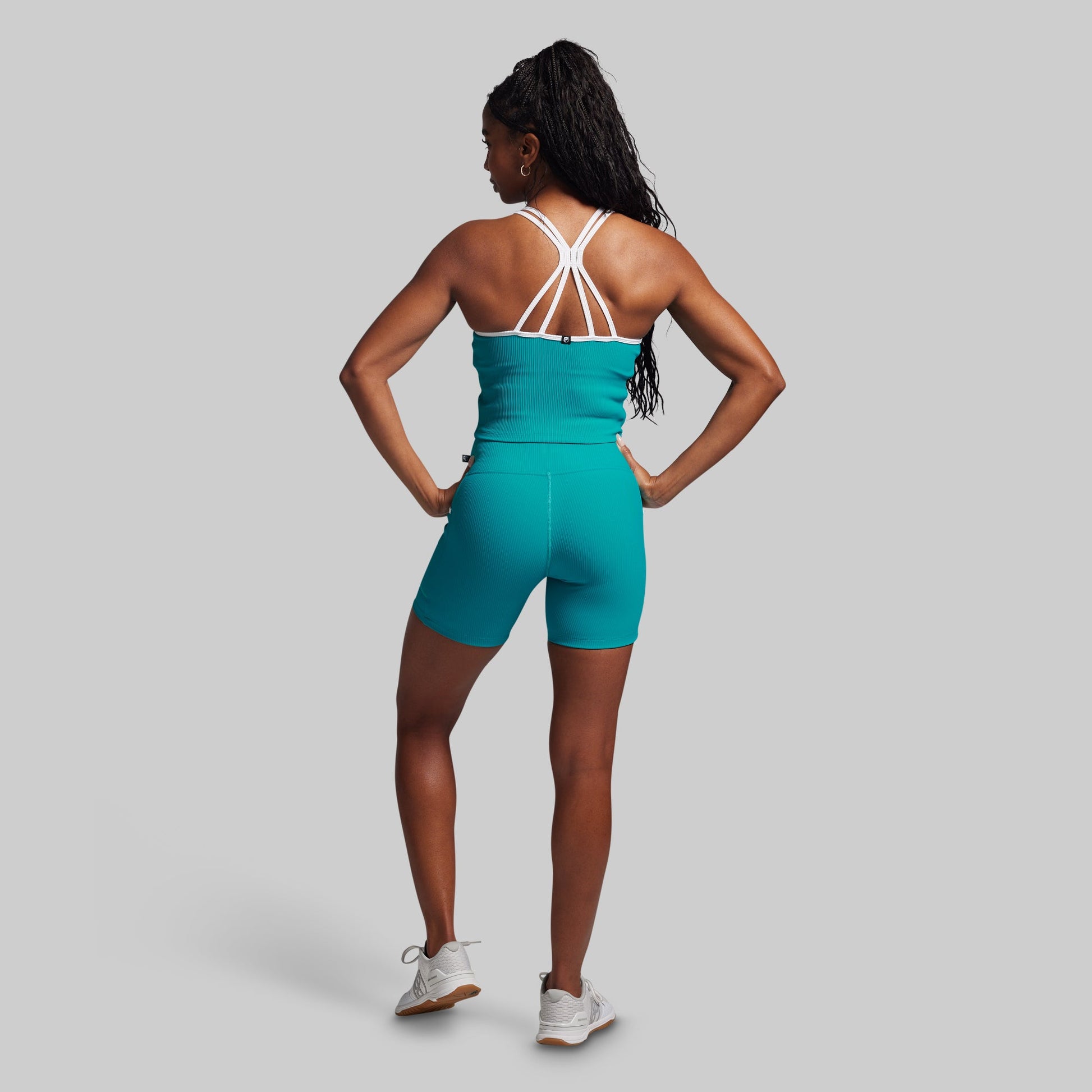 Woman wearing a teal athletic outfit with white straps on a gray background