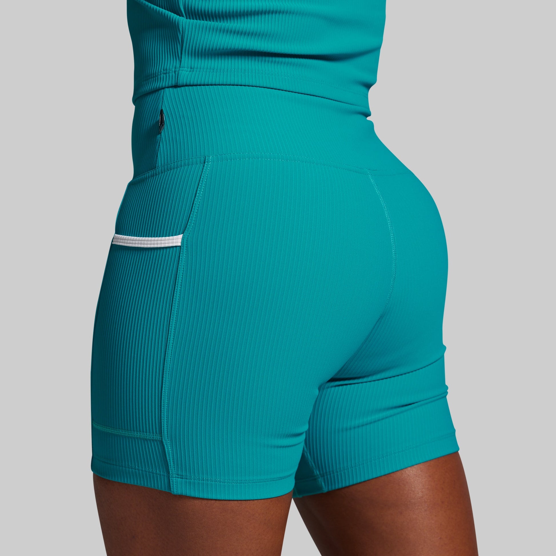 Teal athletic shorts with a pocket on a gray background