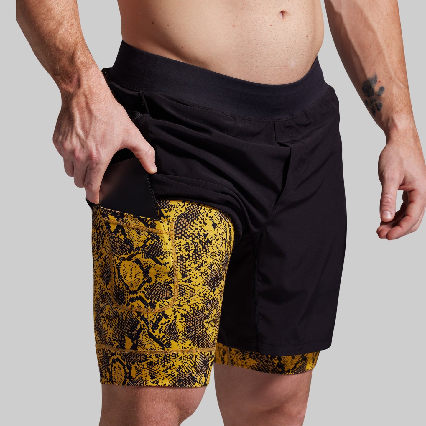 Person wearing black shorts with yellow snake print trim on a plain background