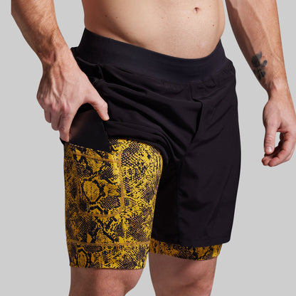 Person wearing black shorts with yellow snake print trim on a plain background