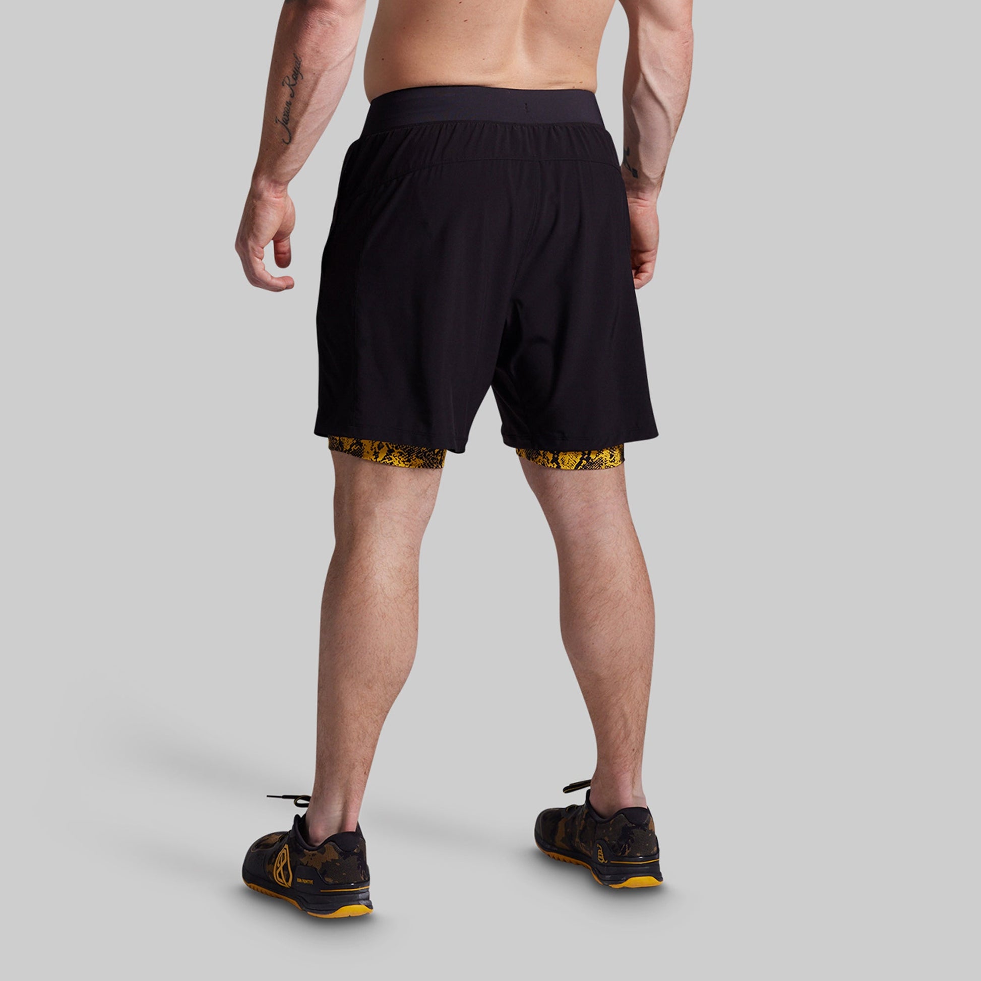 Person wearing black athletic shorts with yellow accents on a gray background