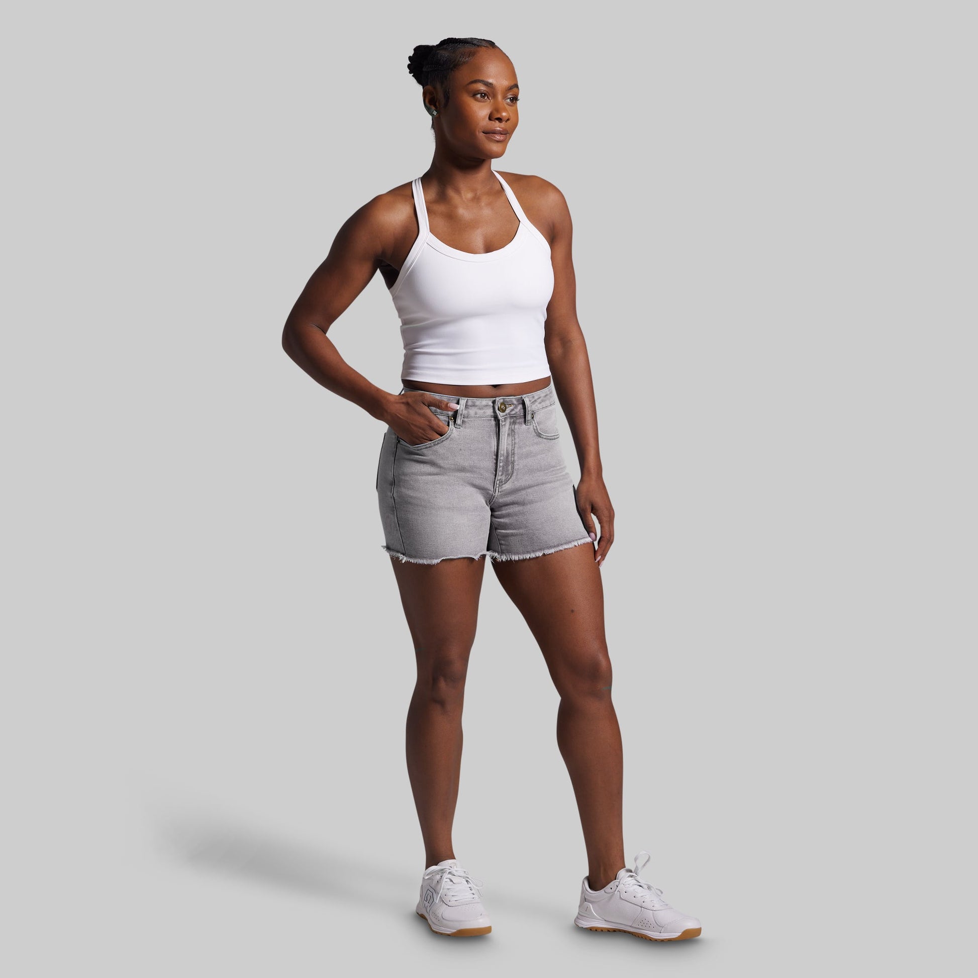 Woman wearing a white tank top and gray shorts on a light gray background