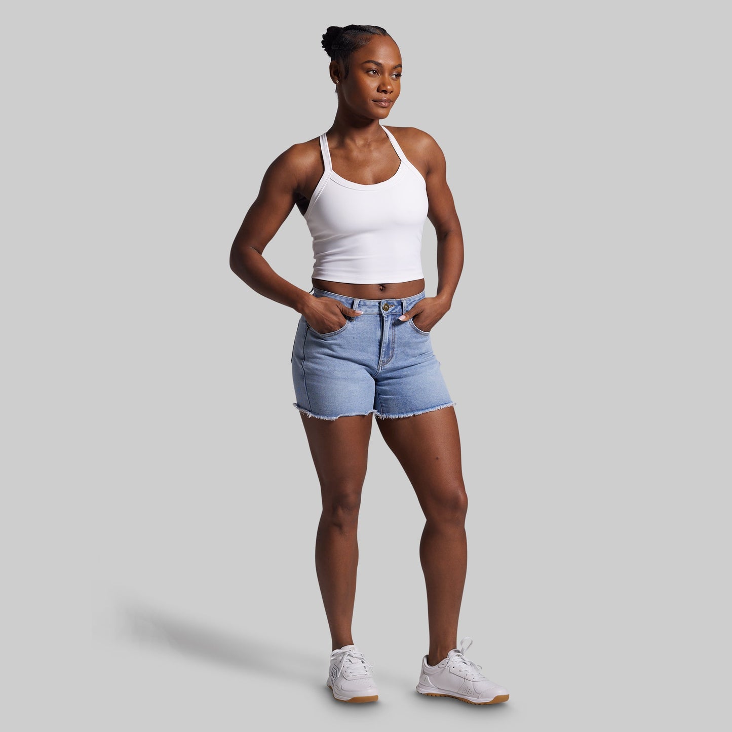 Woman wearing a white tank top and blue denim shorts on a gray background