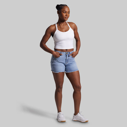 Woman wearing a white tank top and blue denim shorts on a gray background