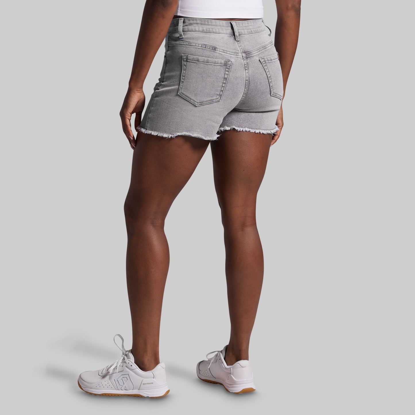 Person wearing gray denim shorts and white sneakers on a light gray background