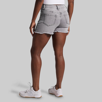 Person wearing gray denim shorts and white sneakers on a light gray background