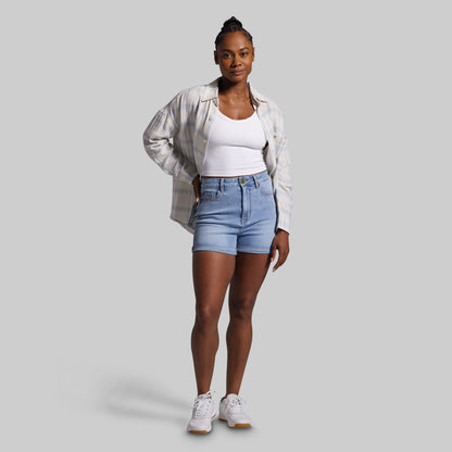 Woman wearing a white shirt, light blue denim shorts, and white sneakers on a gray background