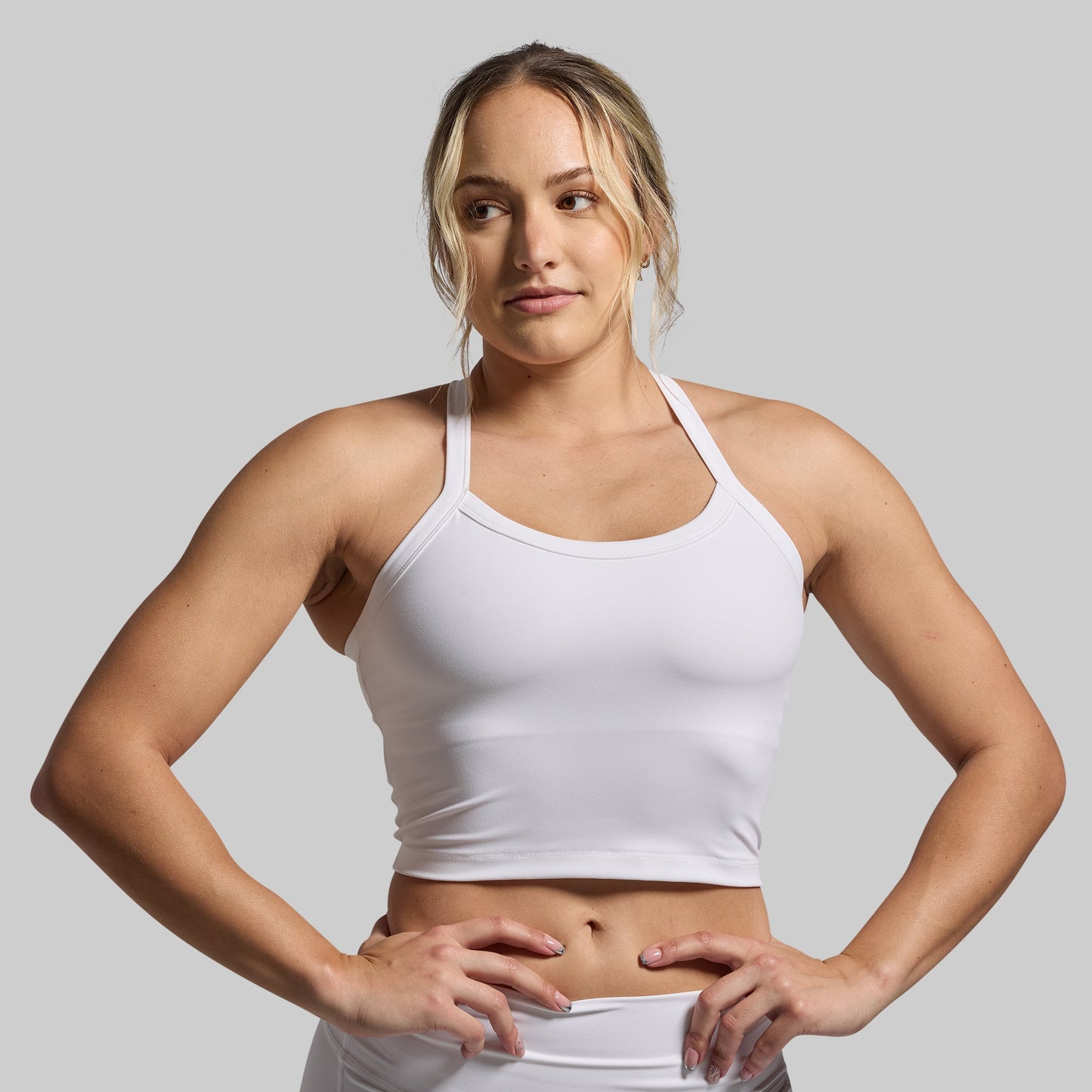 Woman wearing a white sports bra and shorts on a gray background
