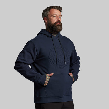 Man wearing a navy blue hoodie with a logo on a gray background