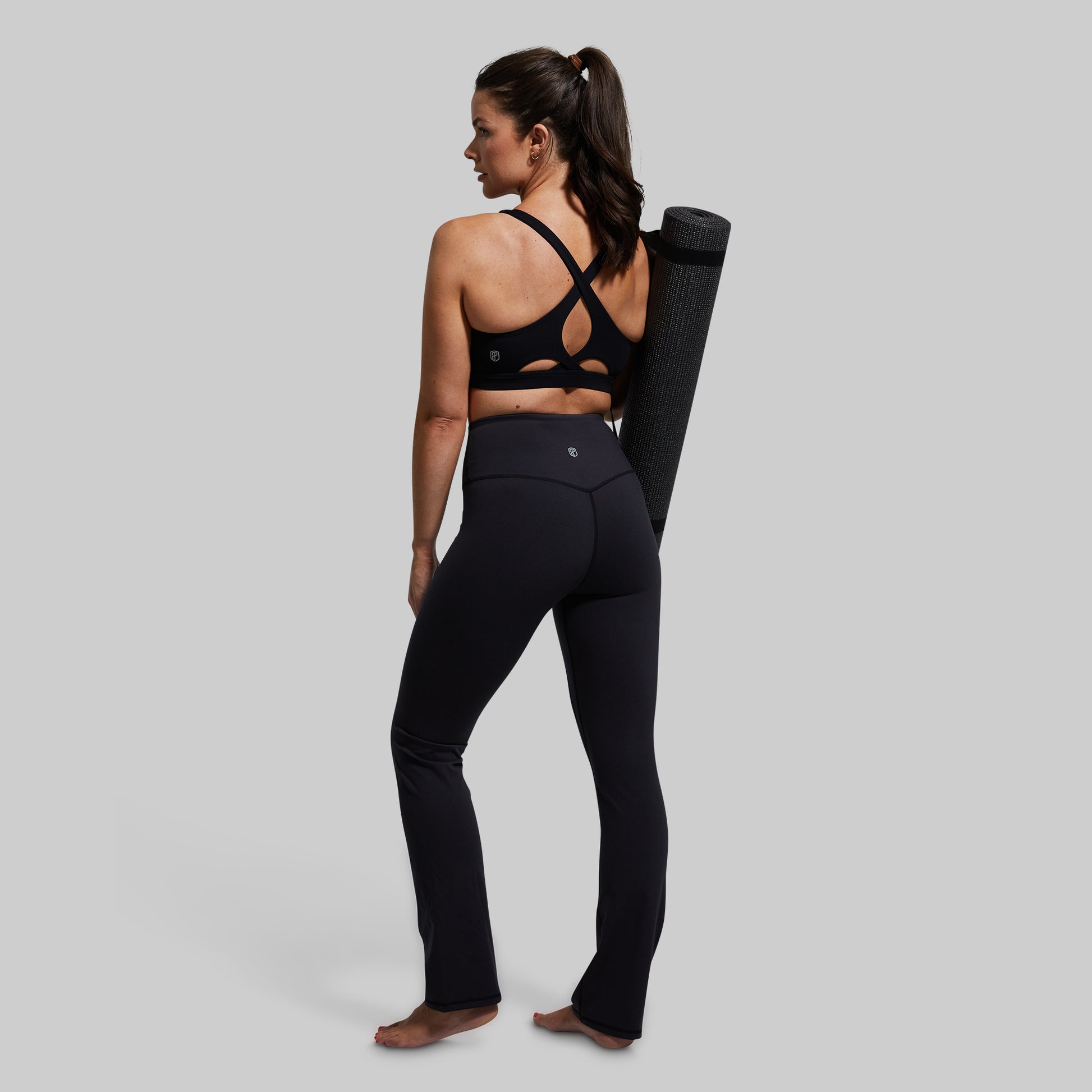 Woman in black athletic wear holding a yoga mat on a plain background