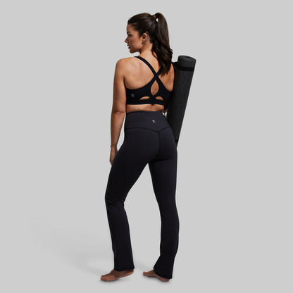 Woman in black athletic wear holding a yoga mat on a plain background