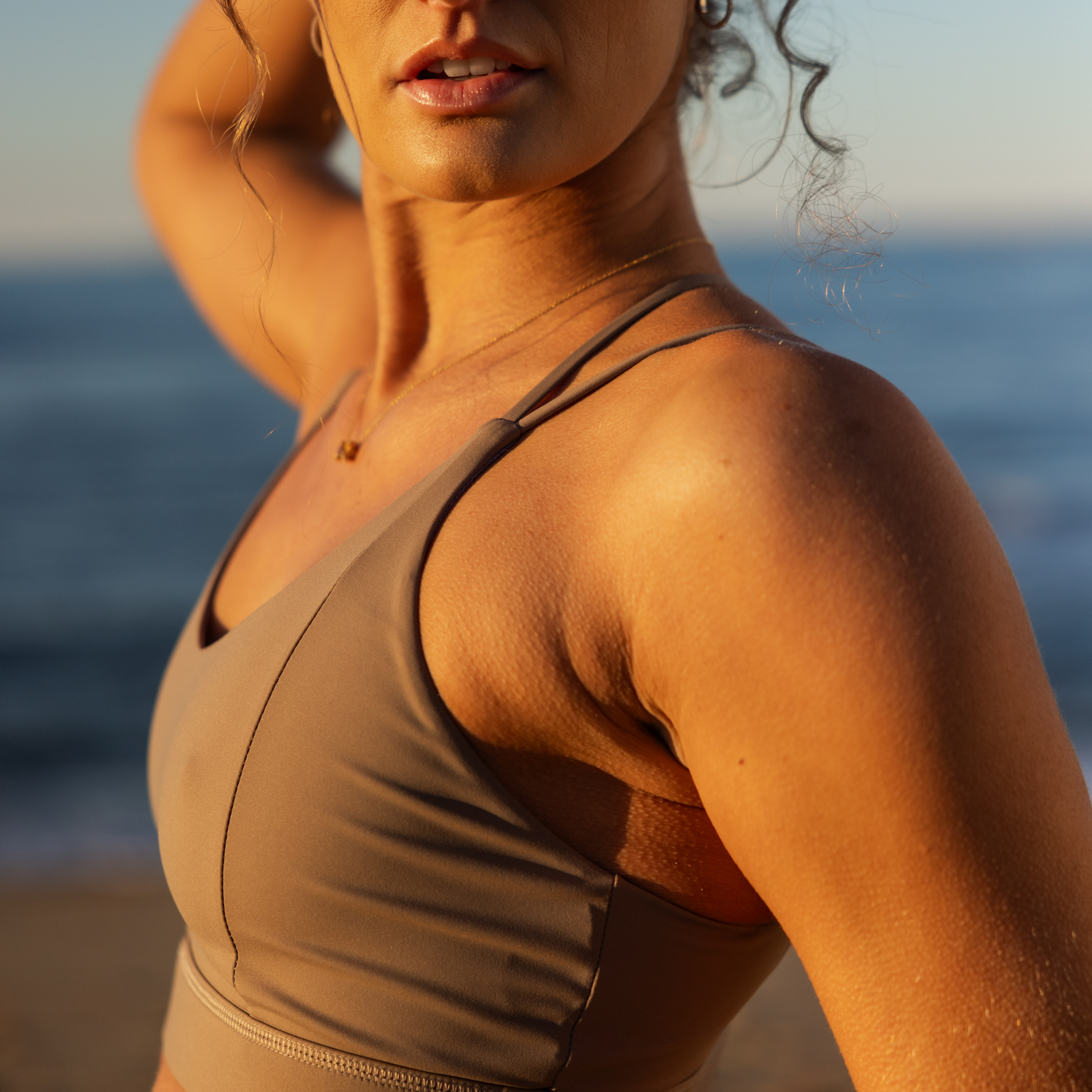 Woman in a brown sports bra standing on a beach with ocean in the background