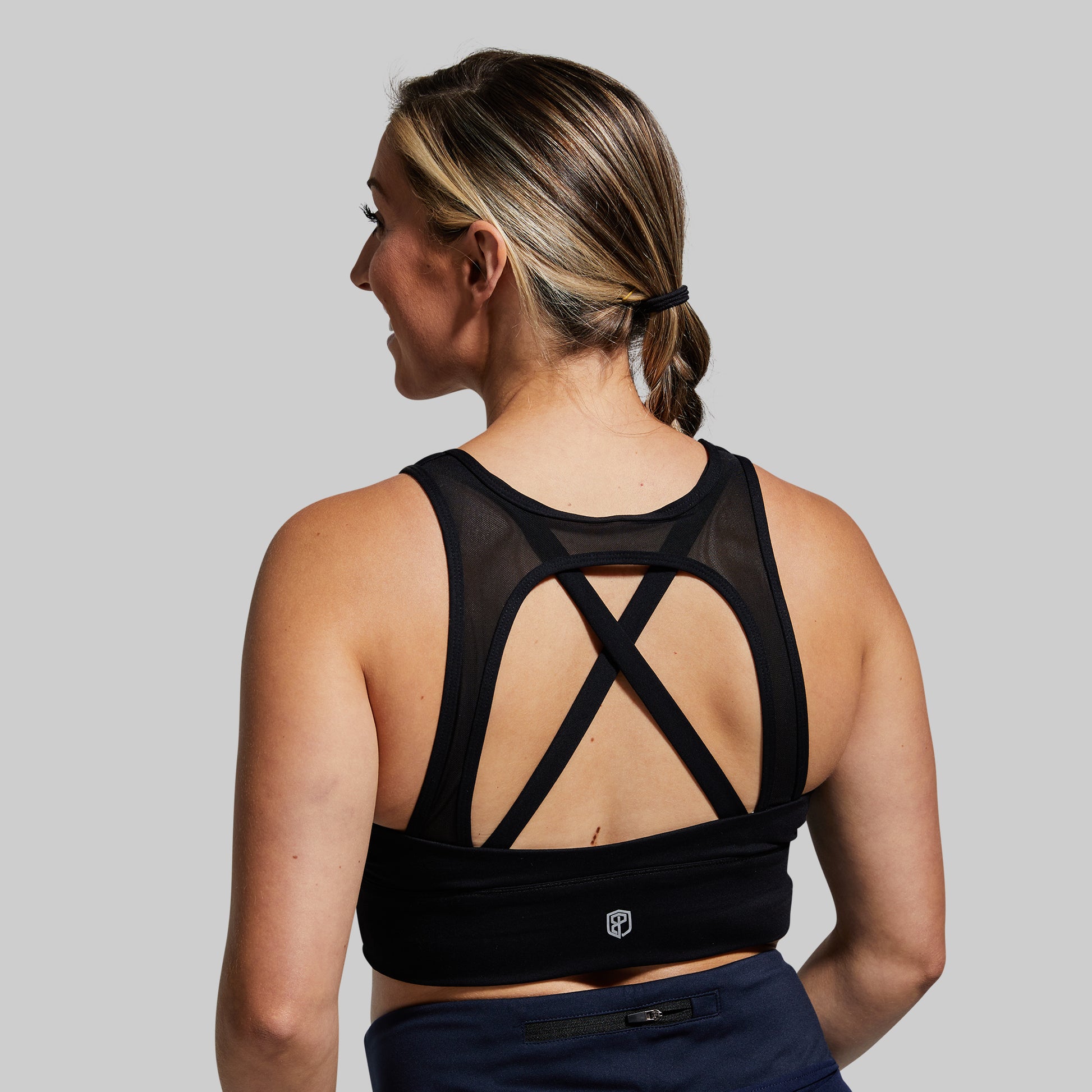 Woman wearing a black sports bra with criss-cross design on a gray background