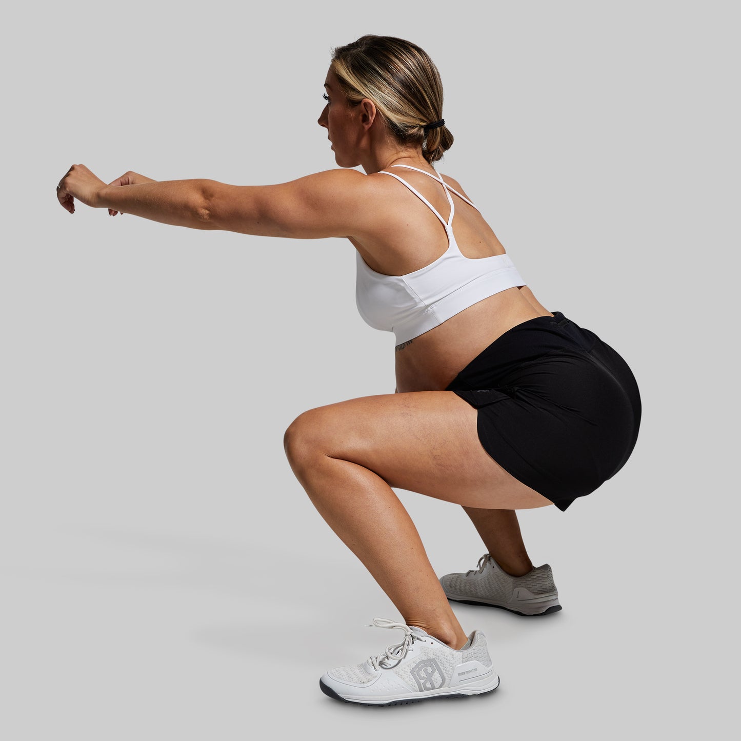 Pregnant woman performing a squat exercise in black maternity shorts on a plain background