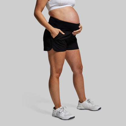 Person wearing black athletic shorts and white sneakers on a gray background