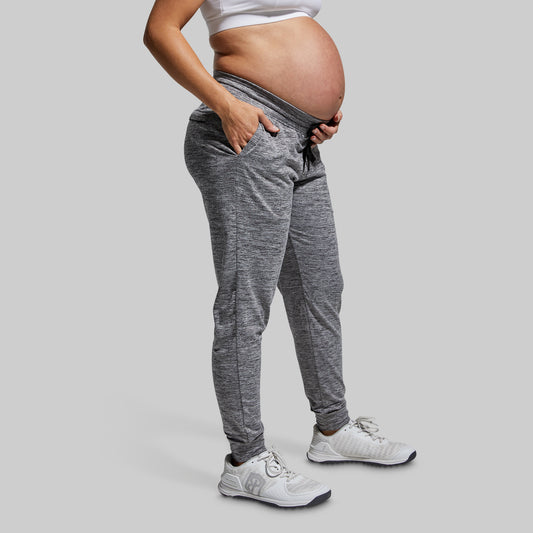 Pregnant person wearing gray jogger pants and white sneakers on a light gray background