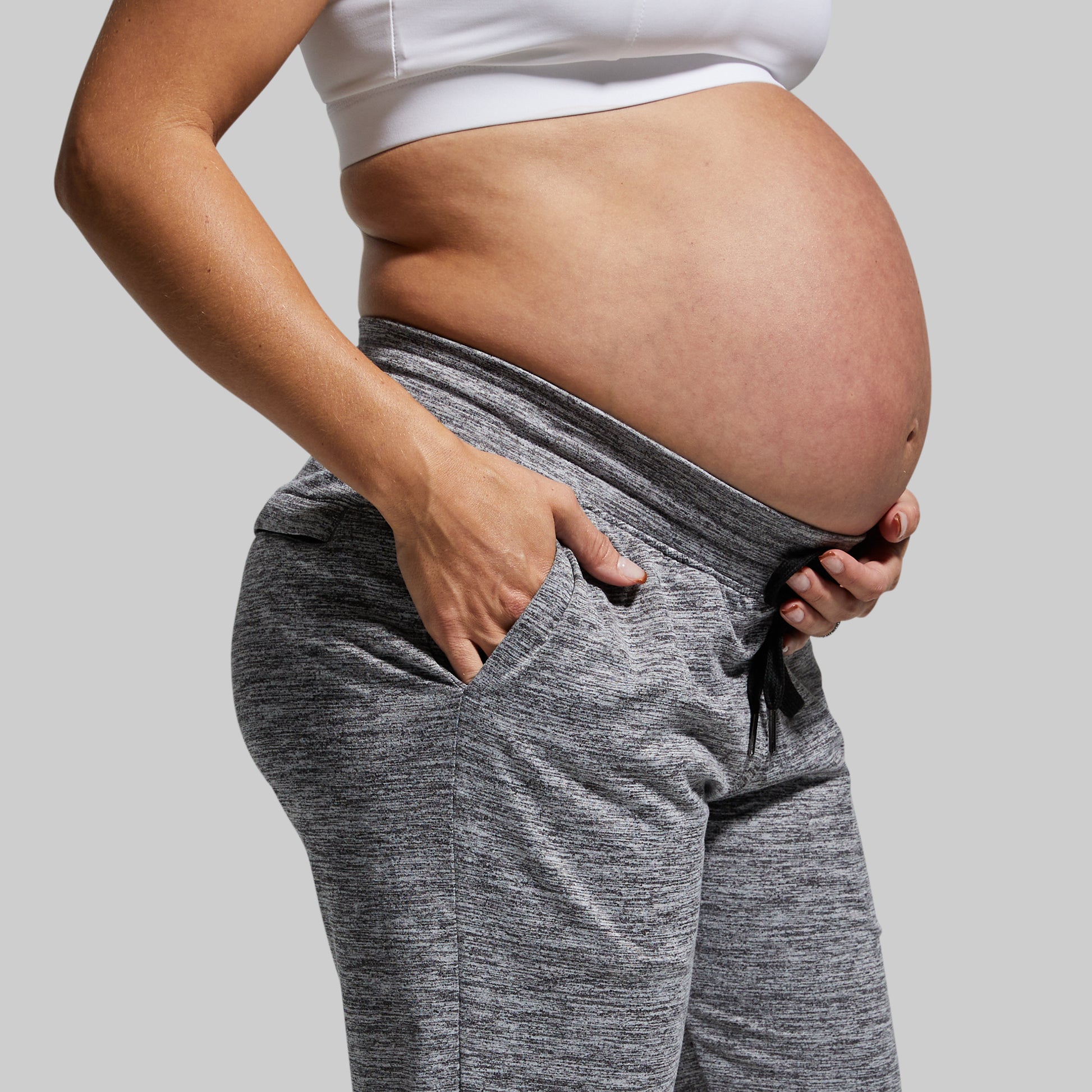 Pregnant person wearing gray sweatpants on a plain background
