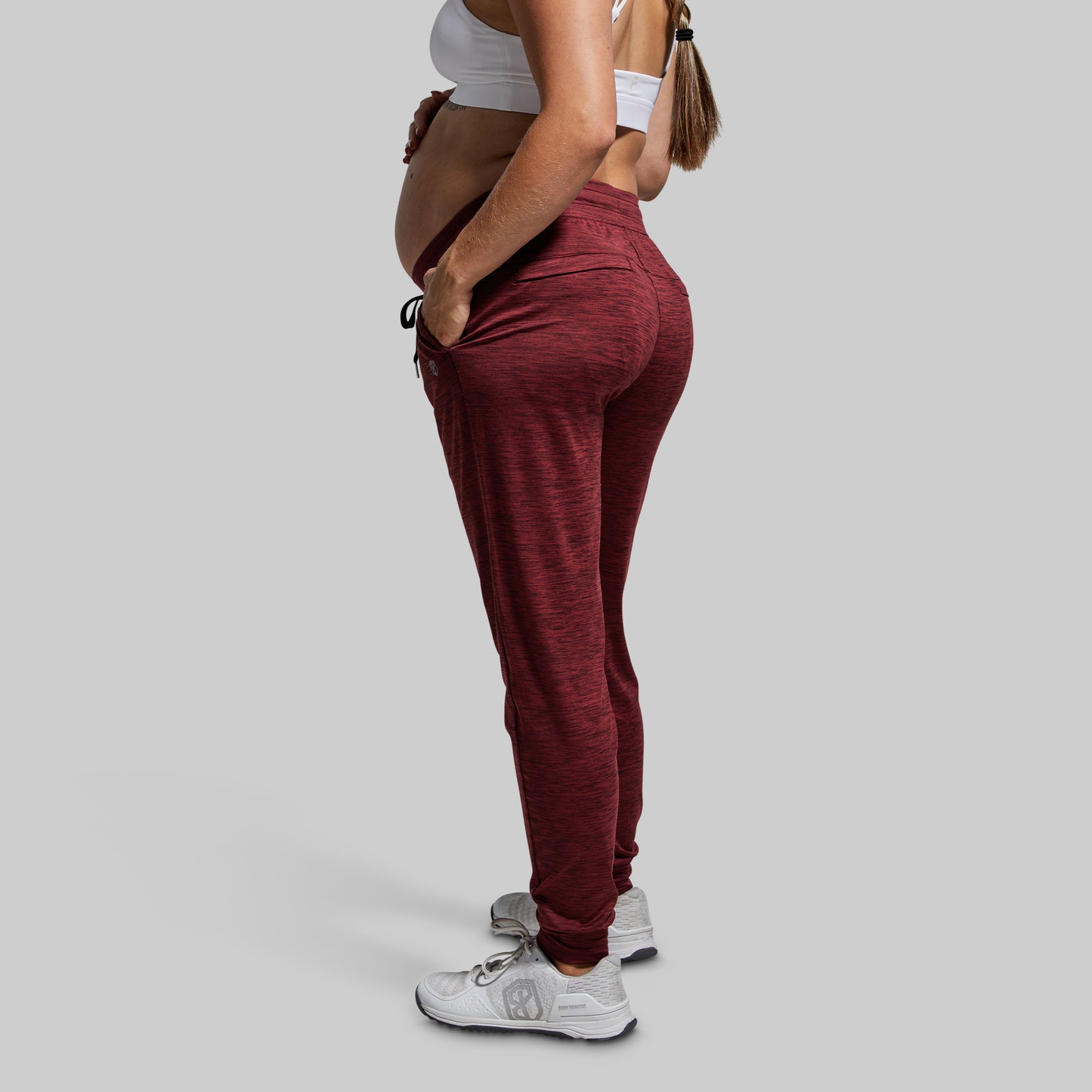 Person wearing maroon jogger pants and a white top on a gray background