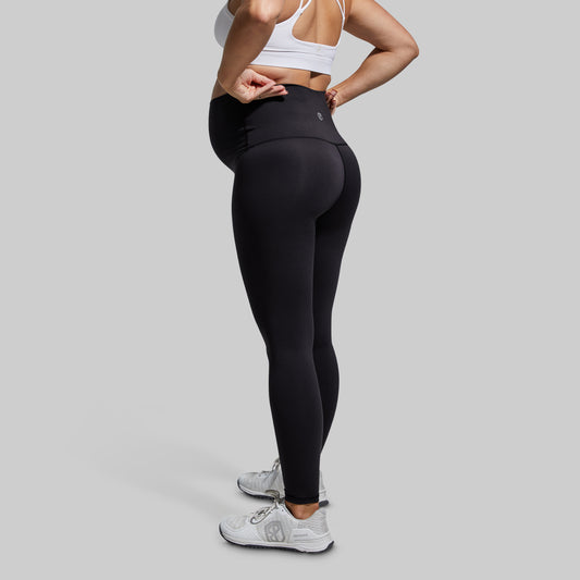 Pregnant person wearing black leggings and a white sports bra on a gray background