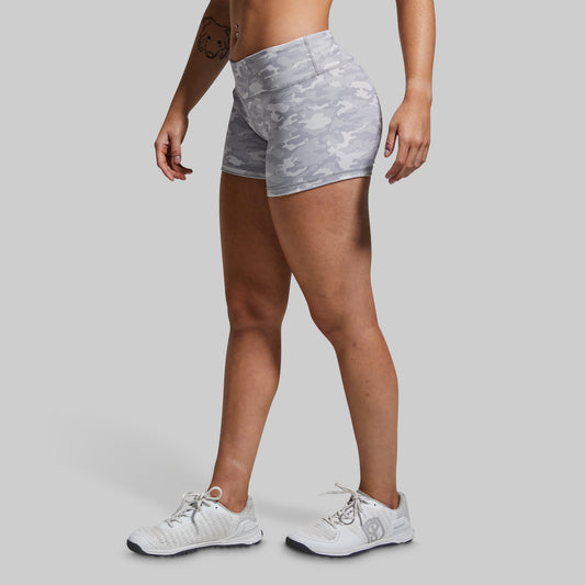 Person wearing gray camouflage shorts and white sneakers on a light gray background