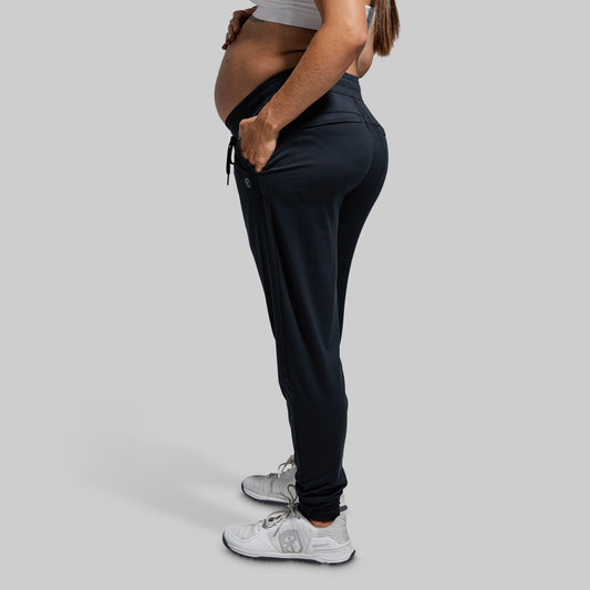 Person wearing black jogger pants and white sneakers on a gray background