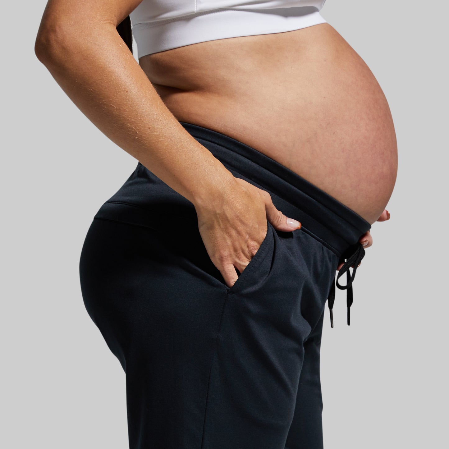 Pregnant person wearing dark jogger pants against a plain background
