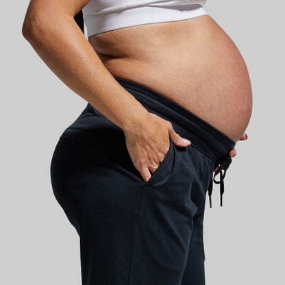 Pregnant person wearing dark jogger pants against a plain background