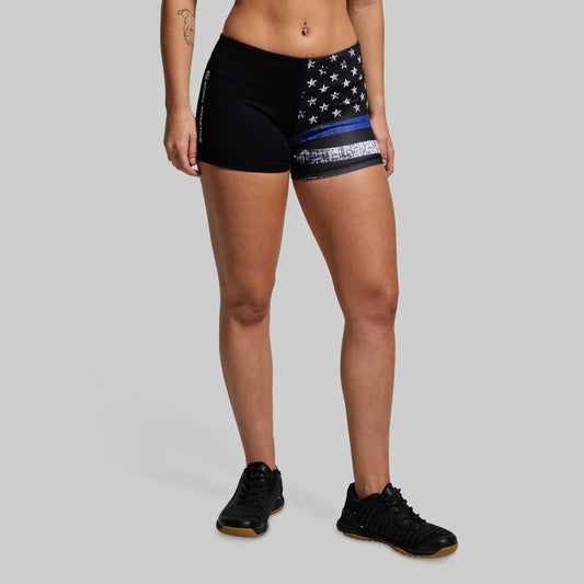 A model wearing black athletic shorts with a distressed American flag design featuring a single blue stripe, paired with black sneakers, against a solid gray background.