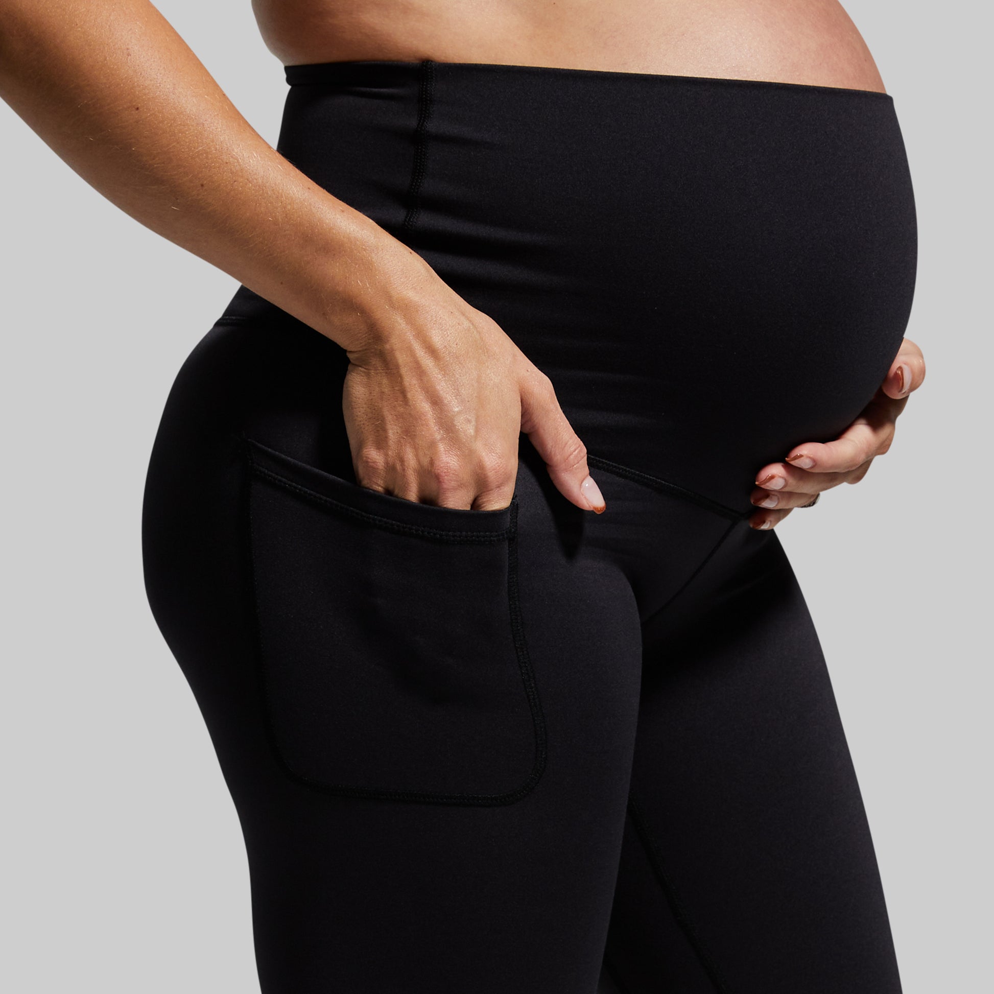 Person wearing black leggings holding their pregnant belly against a gray background