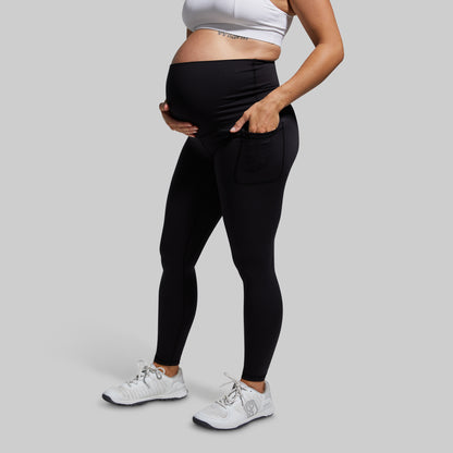 Person wearing black maternity leggings and a white sports bra on a gray background