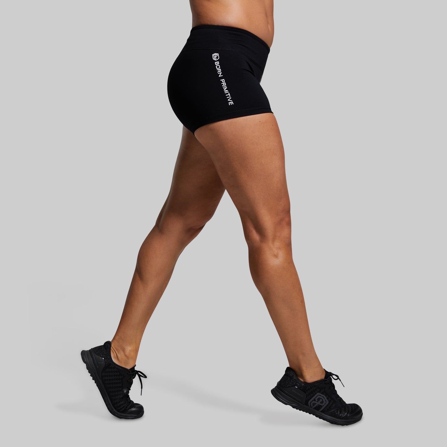 Person wearing black athletic shorts with a brand logo on a gray background