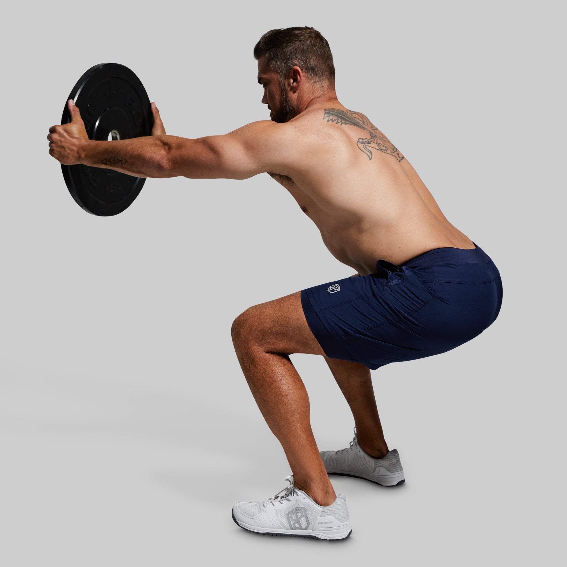 Man performing a squat exercise with a weight plate wearing blue athletic shorts on a gray background
