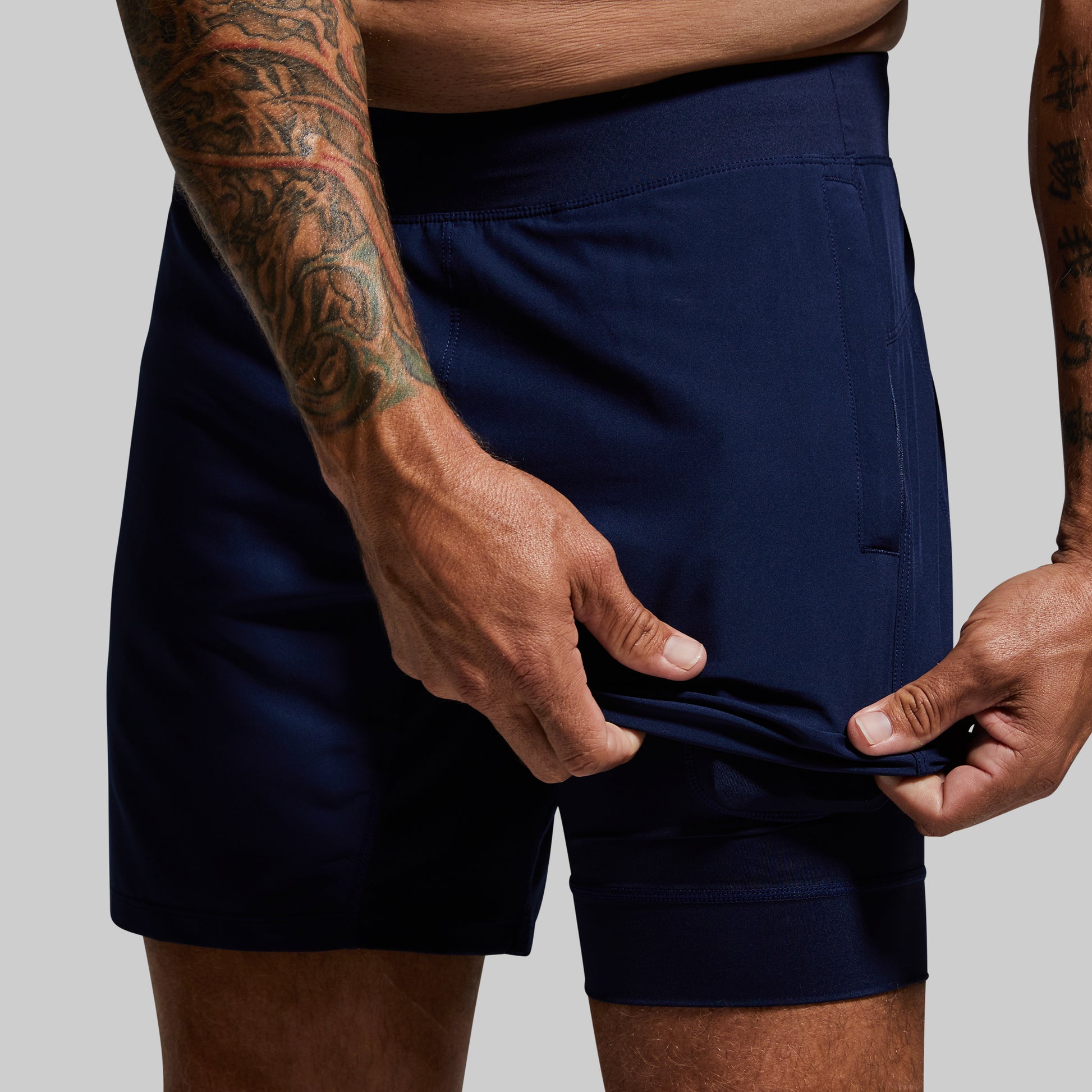 Person wearing navy shorts with visible tattoos on arms, on a plain background