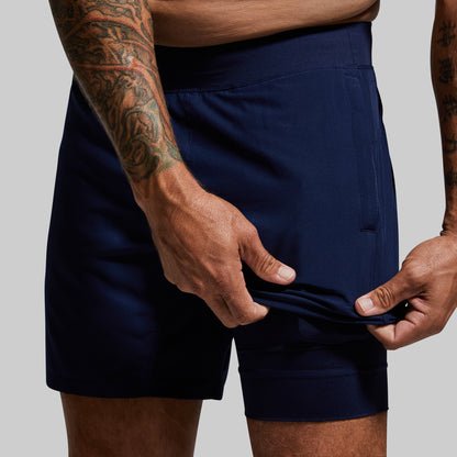 Person wearing navy shorts with visible tattoos on arms, on a plain background
