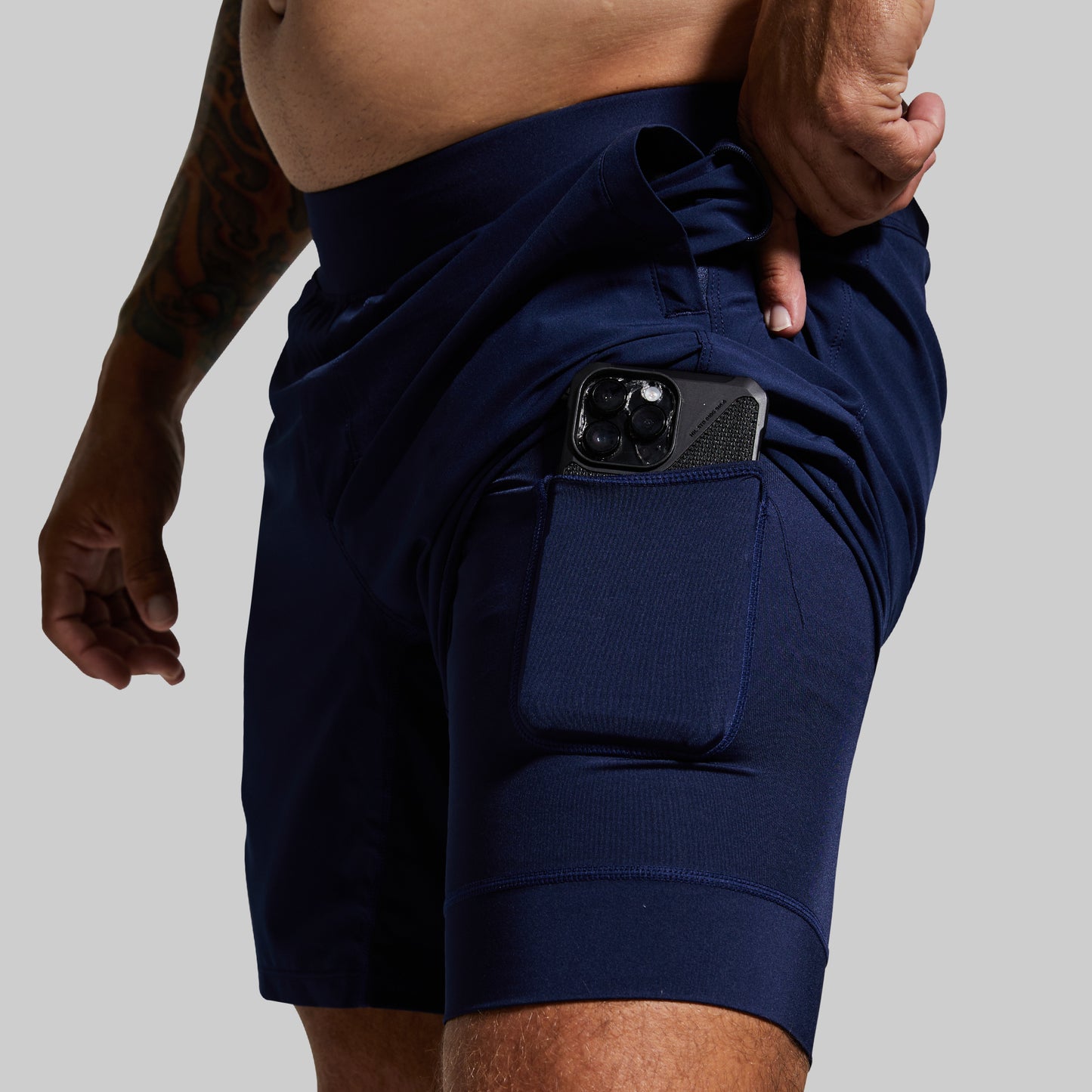 Navy blue athletic shorts with a pocket on a gray background