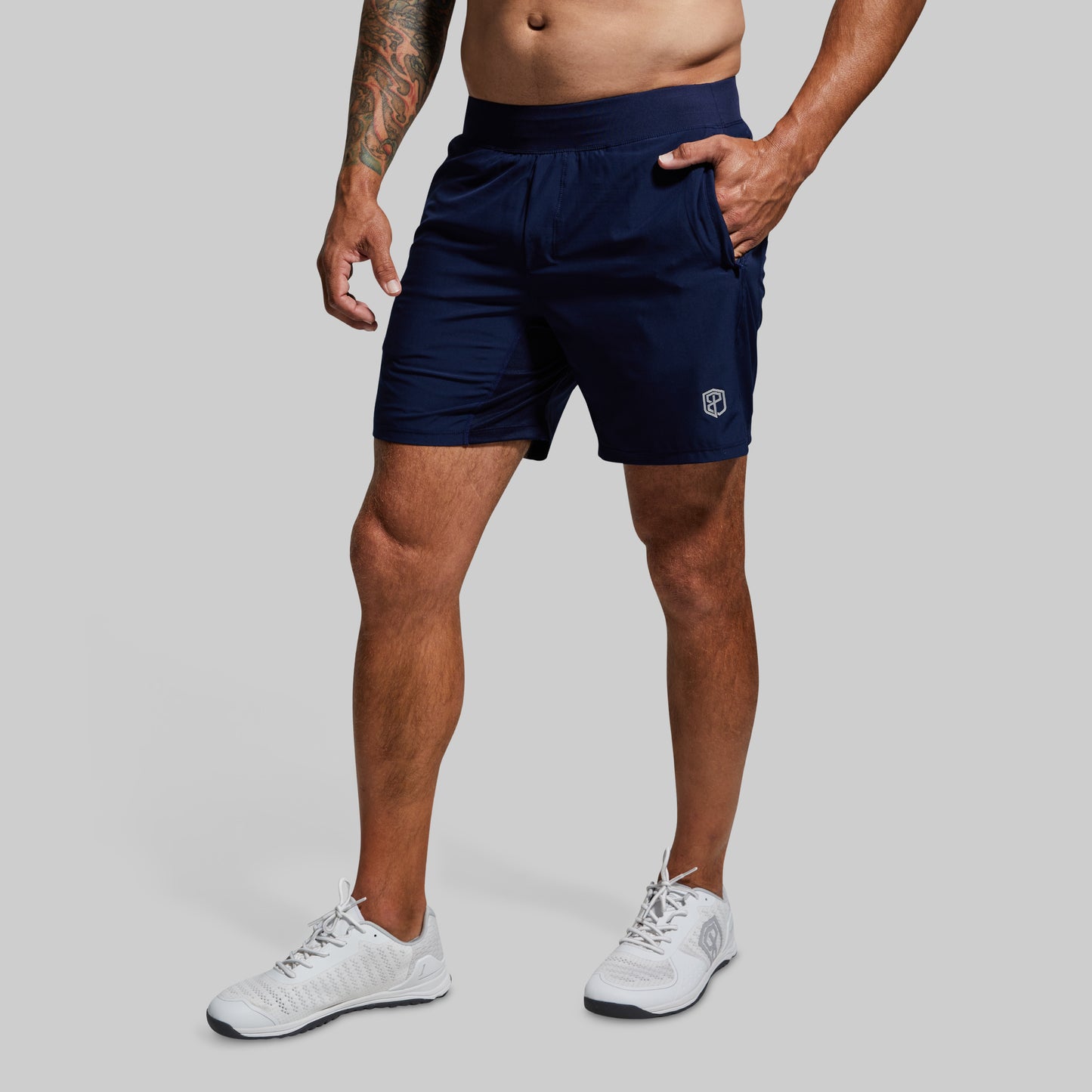 Person wearing navy athletic shorts with a logo on a gray background