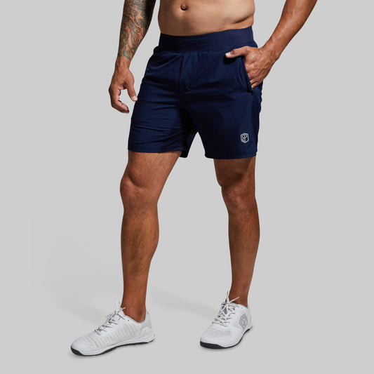 Person wearing navy athletic shorts with a logo on a gray background