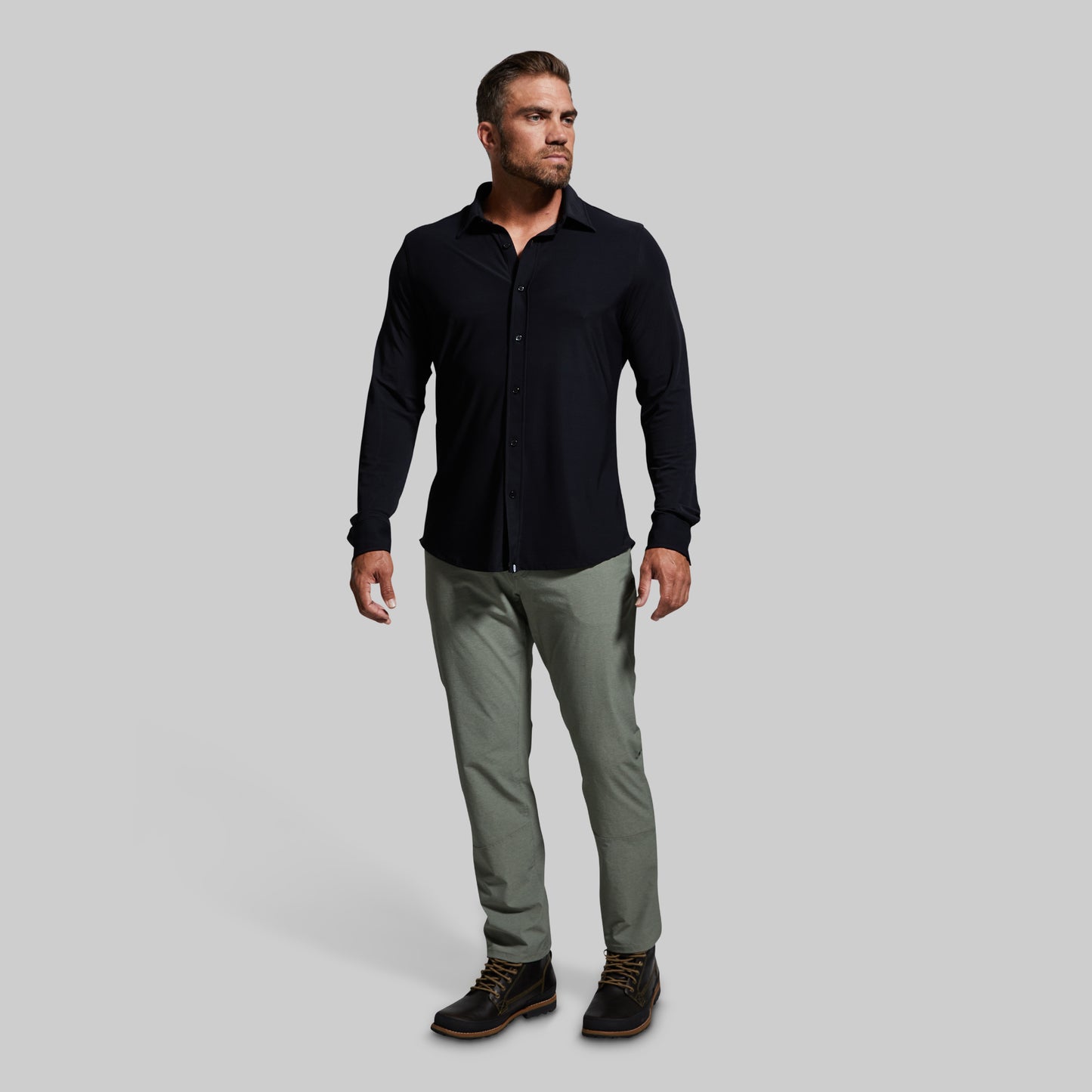 Man wearing a black long-sleeve shirt and gray pants on a light gray background