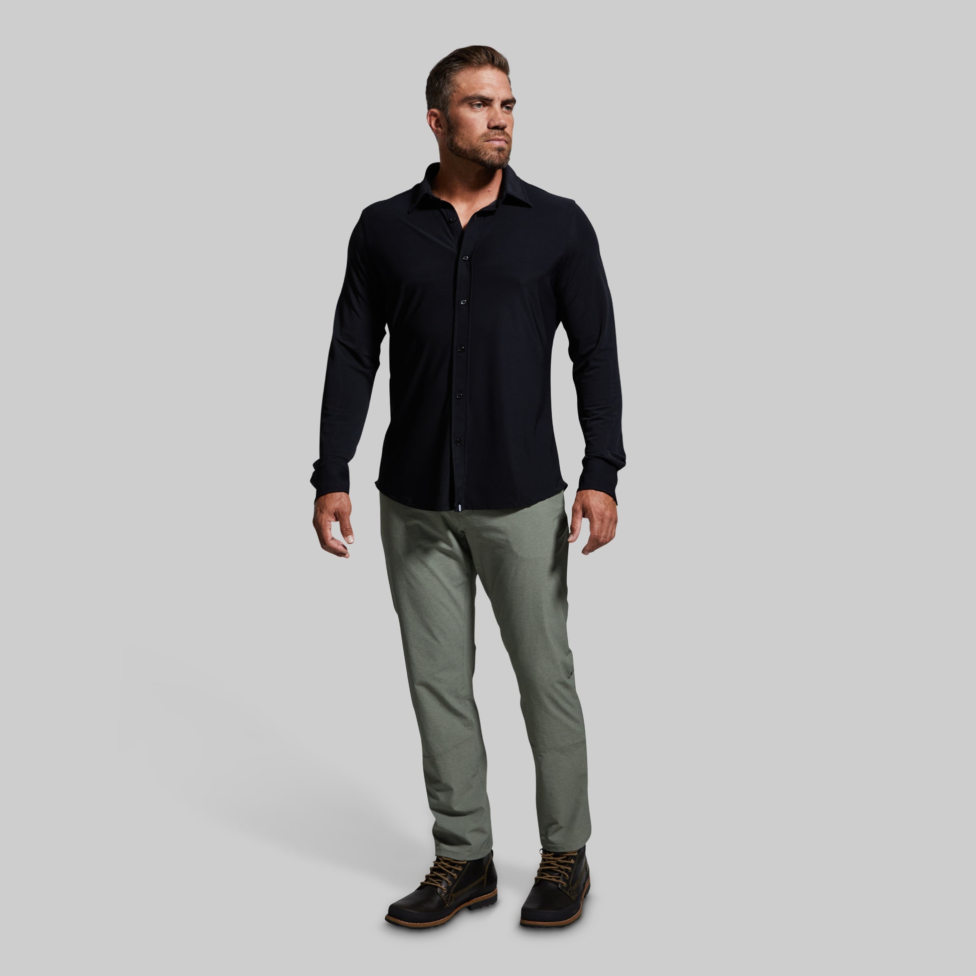 Man wearing a black long-sleeve shirt and gray pants on a light gray background