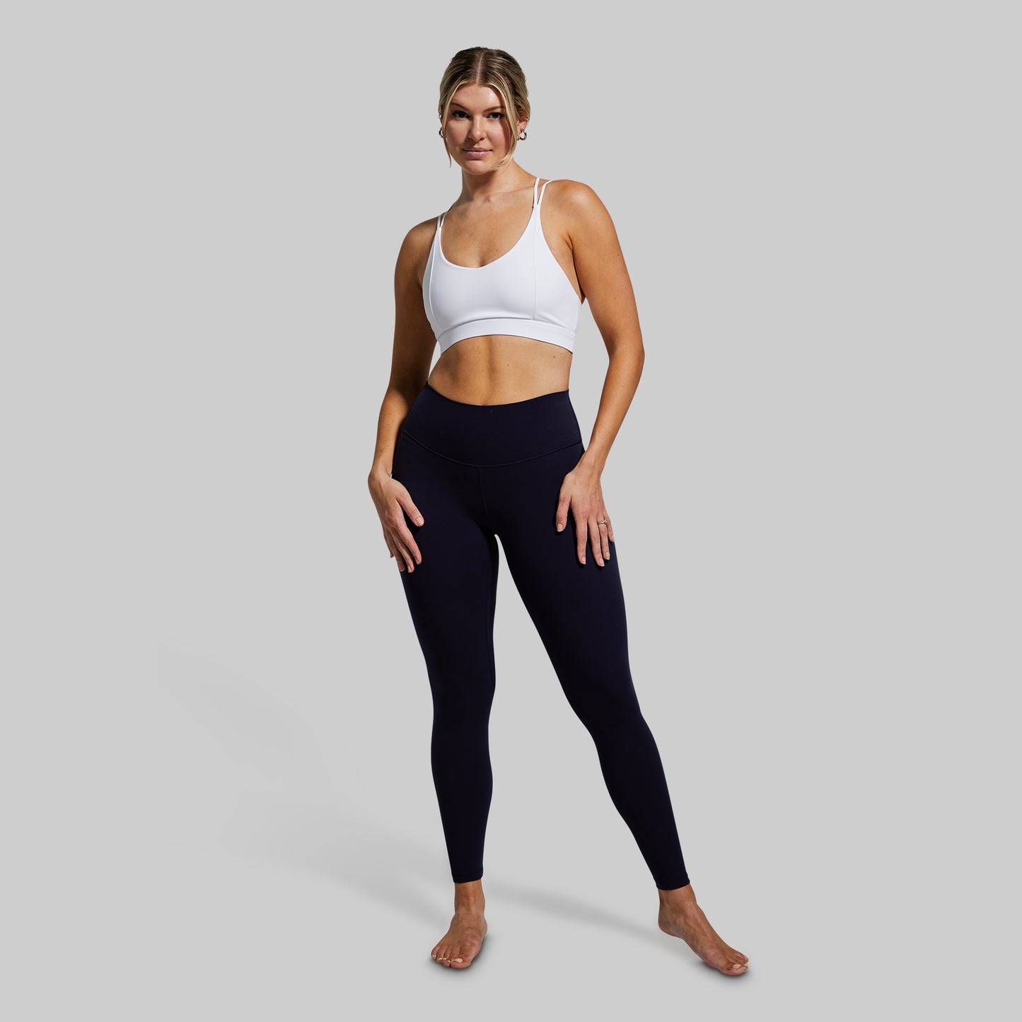 Woman wearing a white sports bra and black leggings on a gray background