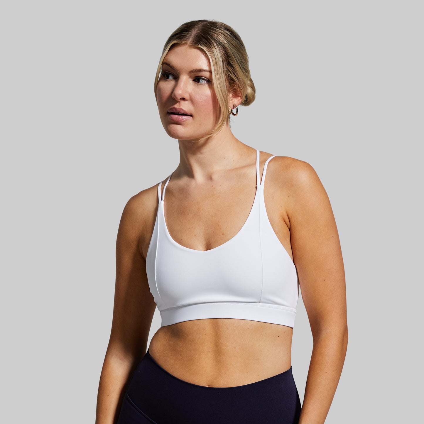 Woman wearing a white sports bra and black leggings against a gray background
