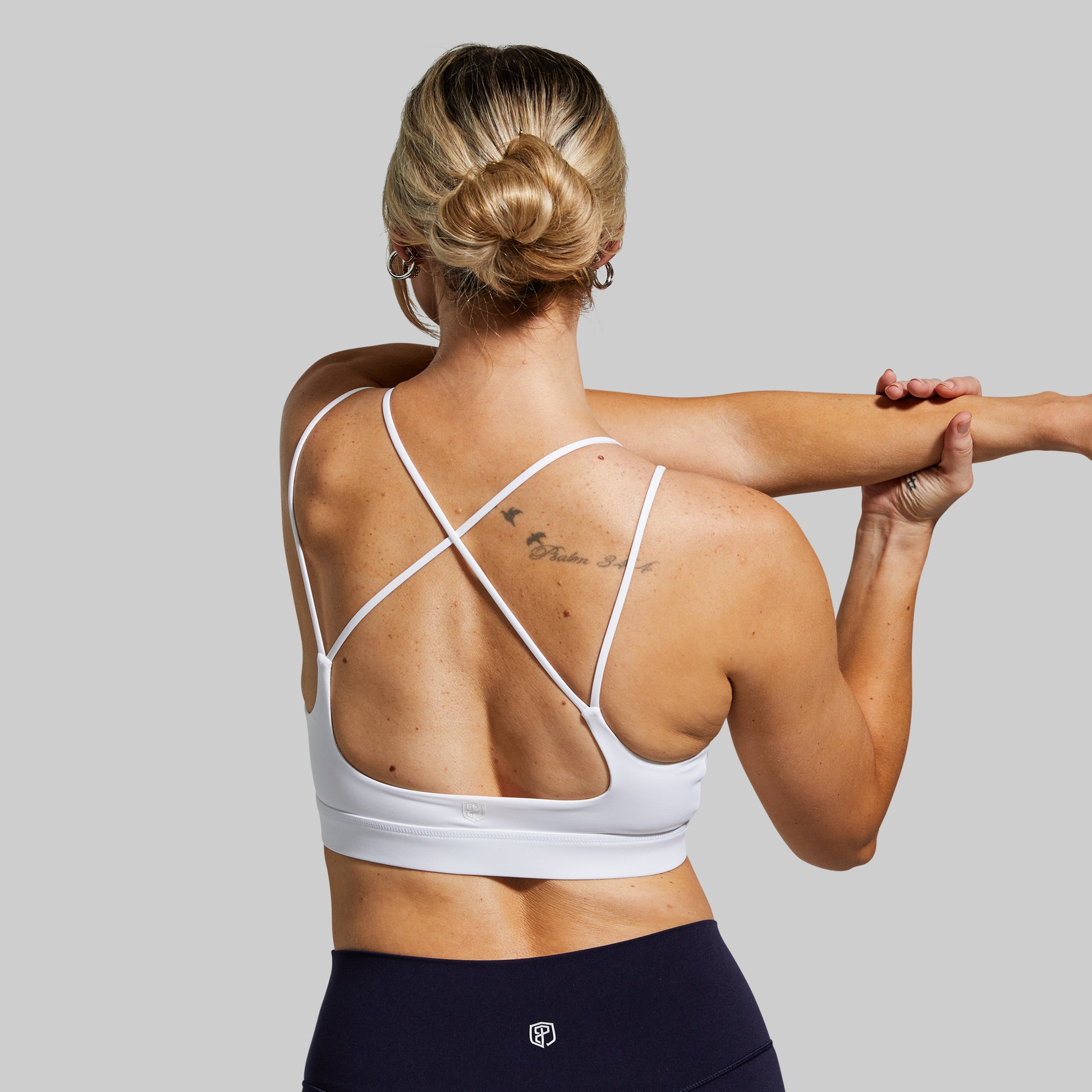Woman wearing a white sports bra and navy leggings on a gray background
